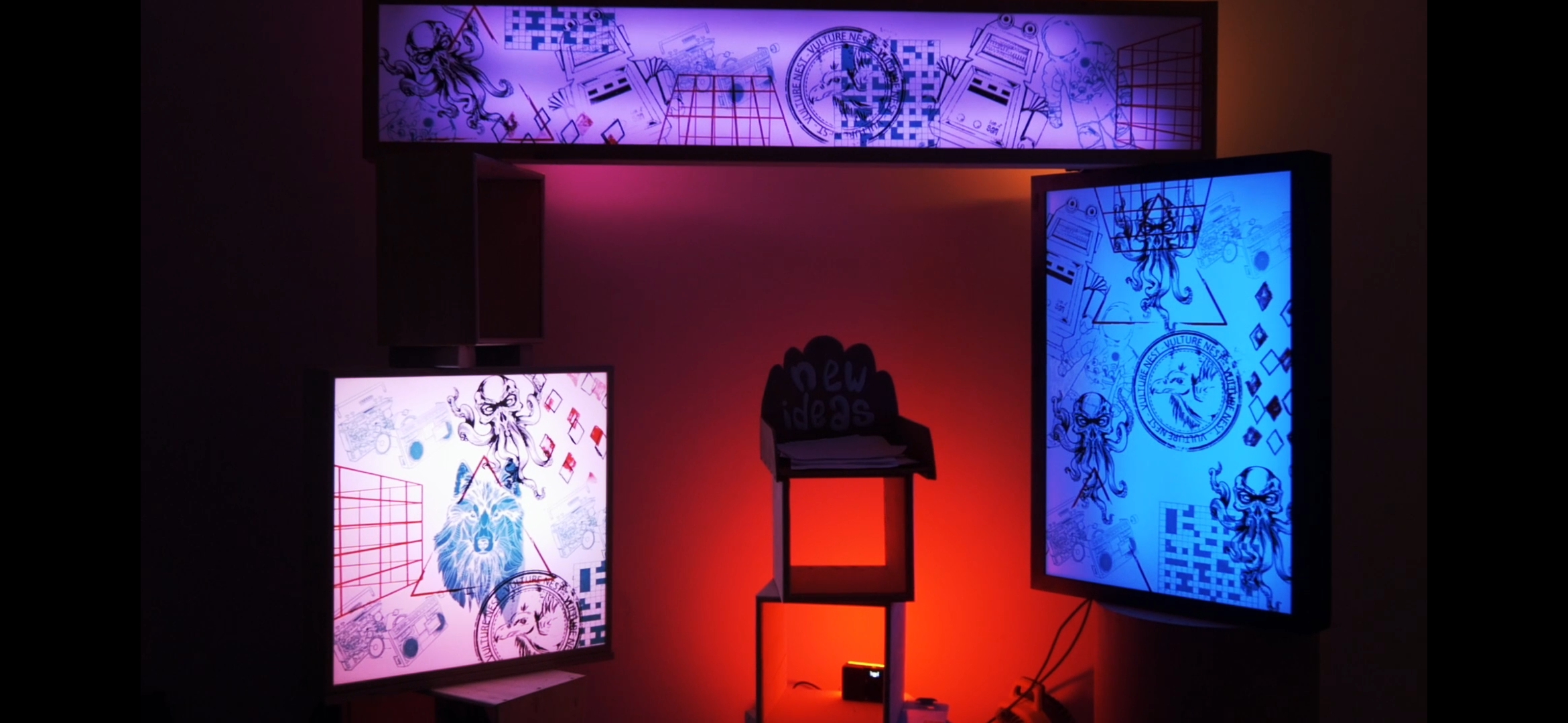 Nicebox multi-piece illuminated installation in warm scene mode: horizontal overhead panel and two upright screen-printed lightboxes glowing cyan and pink against red ambient light, with a hand-cut new ideas plinth sign at centre.