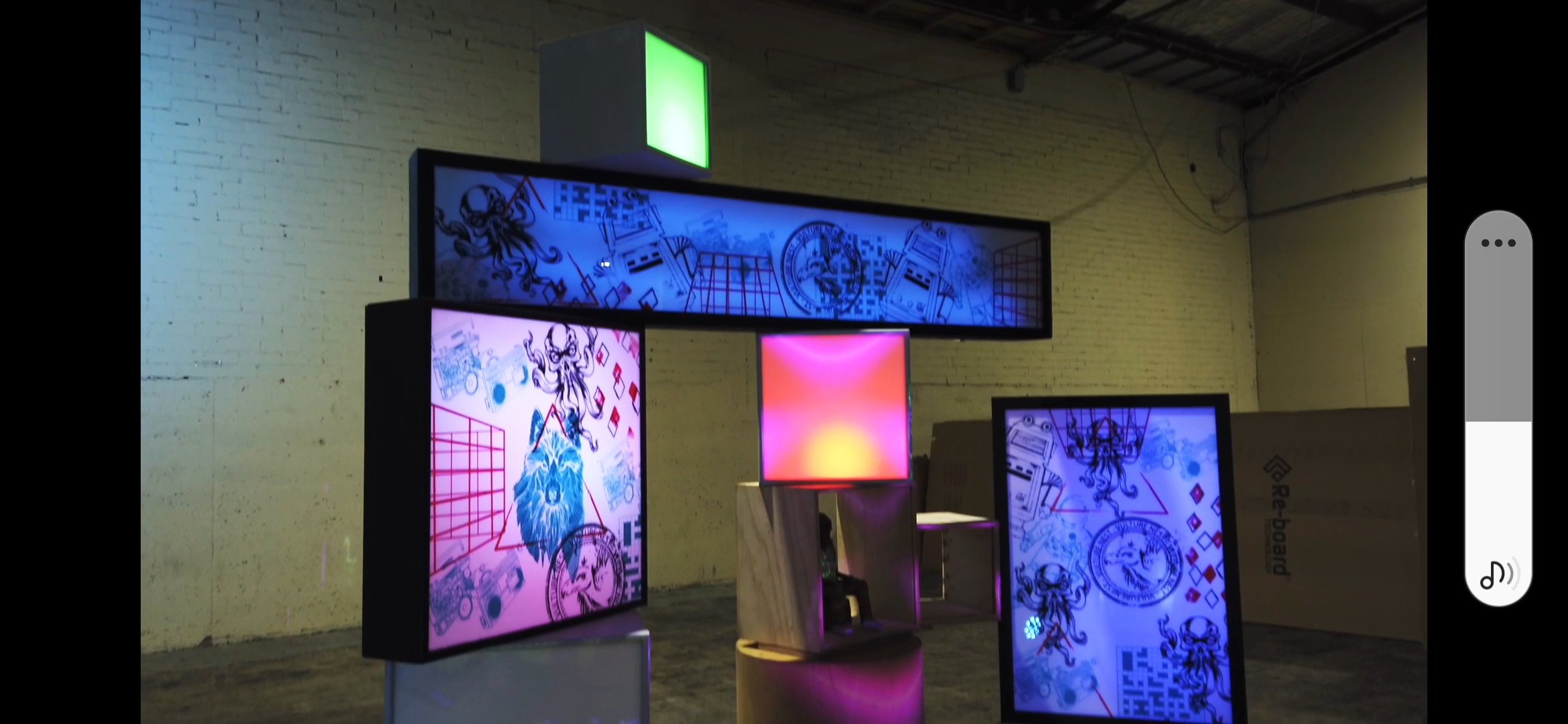 Nicebox multi-piece illuminated installation in a warehouse space: large horizontal panel lightbox, two upright screen-printed panel lightboxes and two solid colour cube lightboxes in green and red-orange, forming an architectural composition.